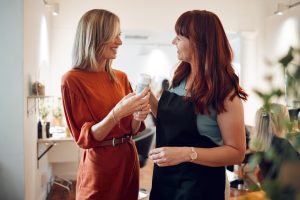 A stylist with their client after an appointment. The stylist is showing their guest a product they suggest to purchase to maintain results at home.